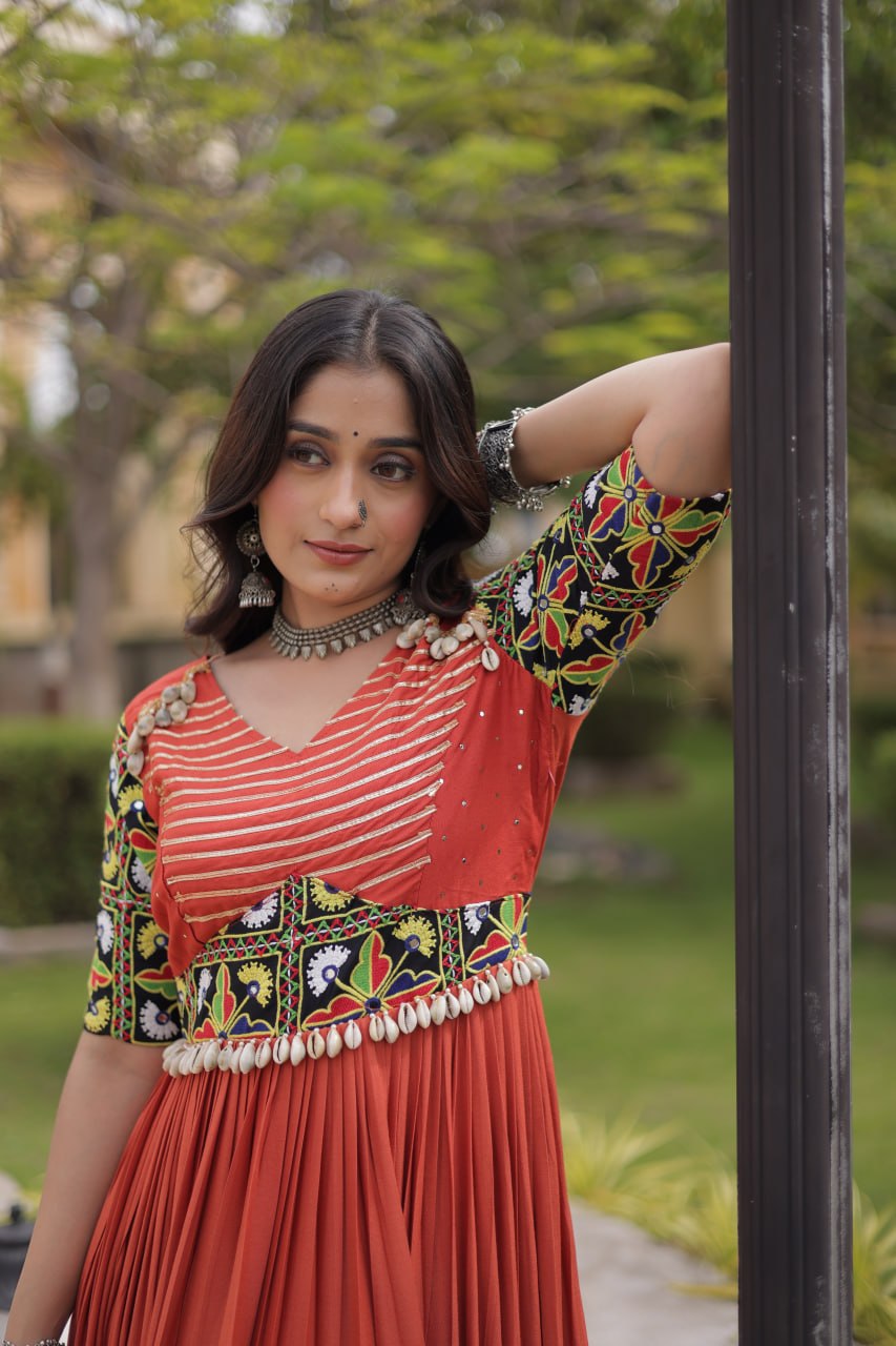 Rust Orange Rayon Navratri Gown With Kutchi Gamthi Thread Embroidery, Mirror Work & Moti Kodi Shell Tassels