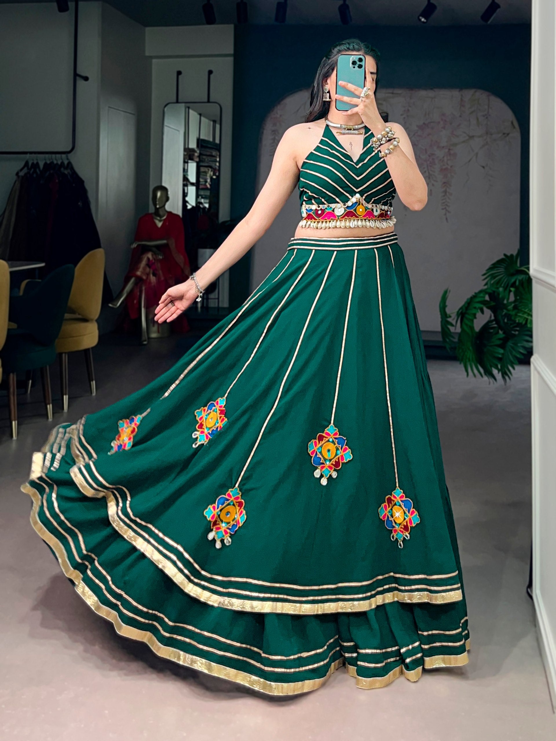 Bottle Green lightweight Navratri lehenga choli featuring vertical gotta patti lines, multi-color gamthi work patches, mirror detailing, and a halter neck blouse with shell tassels by The Beauty Queen