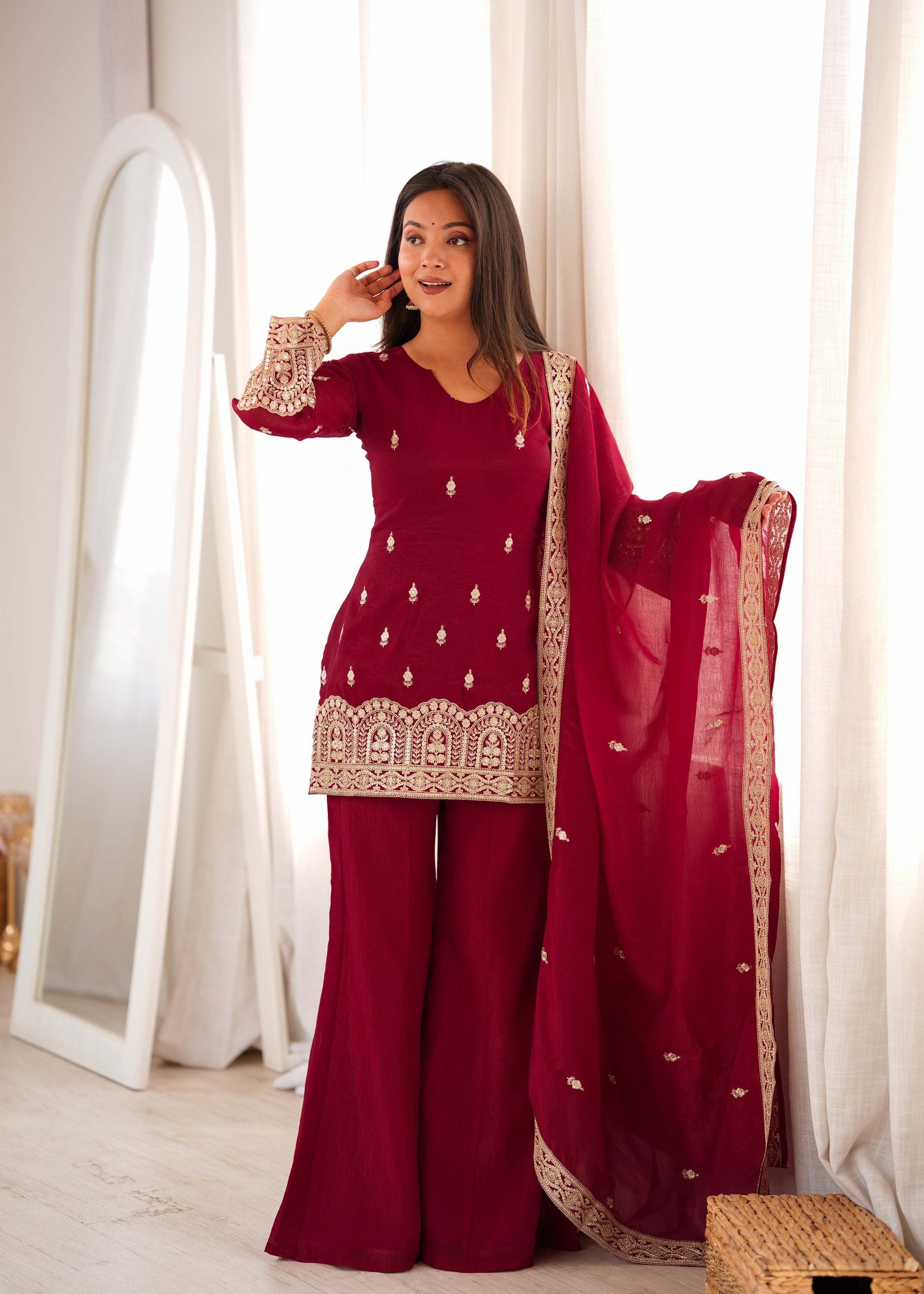 Model posing in a Burgundy Maroon Crunch Silk Kurti Sharara Suit Set with Heavy Sequin, Dori, and Zari Embroidery Borders and Fancy Back Dori by The Beauty Queen