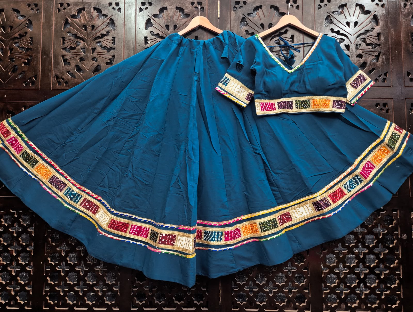 Flat-lay display of a Peacock Teal Blue Pure Cotton Navratri Kalidar Flared Lehenga Choli with Multi-Color Bandhani Patchwork Border and Gold Gota Patti Lace by The Beauty Queen