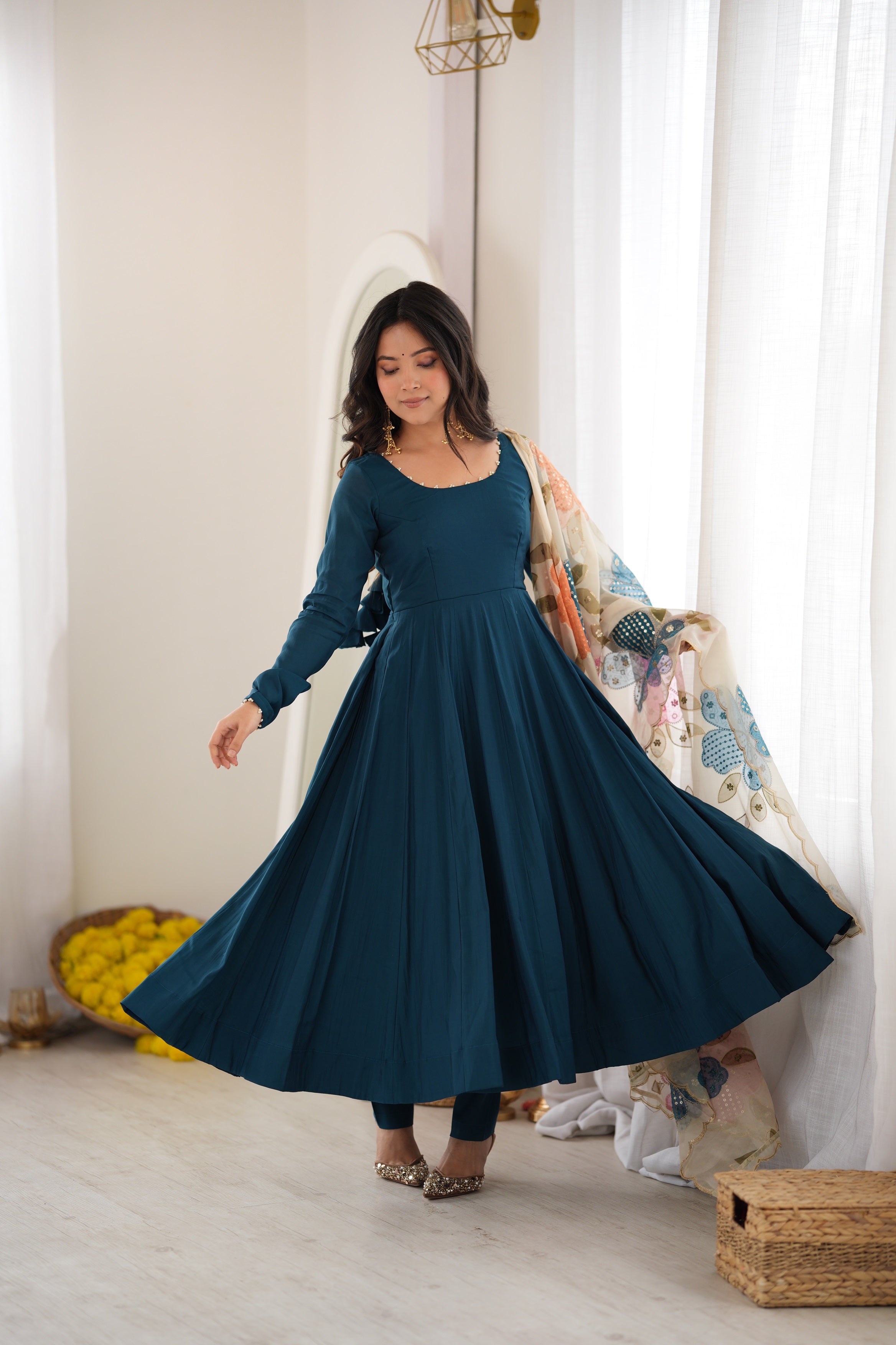 Model twirling in a Peacock Teal Blue Heavy Pure Roman Silk Fully Flared Anarkali Gown Set with Pearl Neckline and Floral Appliqué Organza Dupatta by The Beauty Queen