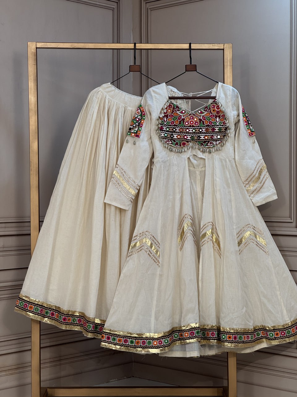 Pristine Off-White Ivory Kora Cotton Navratri Special Flared Lehenga Choli Set with Gujarati Gamthi Embroidery, Cowrie Shell Trims, Chevron Gota Patti & Long Flared Kedia Style Angrakha Top